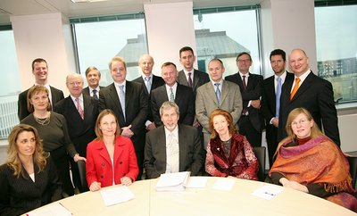 Men and women in formal clothing gather for a picture, with some sitting at a table and others behind them